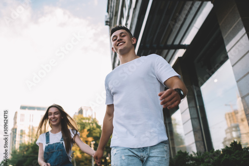 Below view of happy hipster guy dressed in casual wear holding hand of cheerful girlfriend and exploring city area togetherness, positive male and female walking and laughing feeling good from getaway #309624715