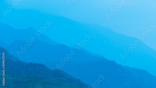 silhouettes of mountains in blue haze. Outline of gentle hills in the valley © Koirill