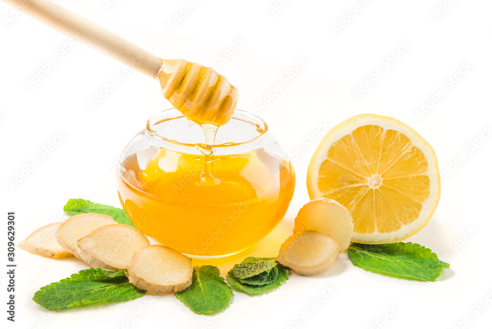 Glass jar of honey and dipper with ginger, mint, carnation, cinnamon and lemon isolated on a white background with space for text Glass jar of honey and dipper with ginger, mint, carnation, cinnamon and lemon isolated on a white background with space for text