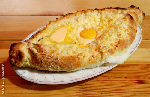 Plate of Adjaruli Khachapuri, Traditional Georgian Cheese and Egg Bread Served on Wooden Table