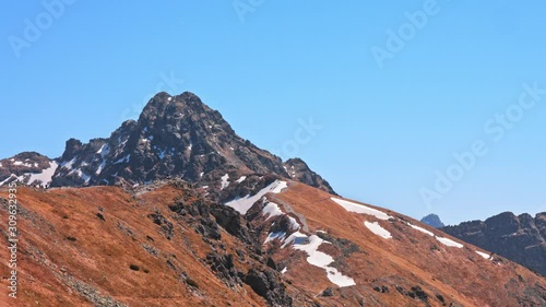Landscape of Polish mountain range Tatry with peaks covered with snow, travel routes and people hikers making way on clear sunny day with blue sky. Hiking activity, travel in mountains concept