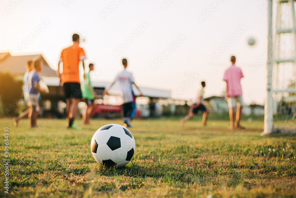 Fototapeta premium Silhouette action sport outdoors of diversity of kids having fun playing soccer football for exercise in community rural area under the twilight sunset sky.