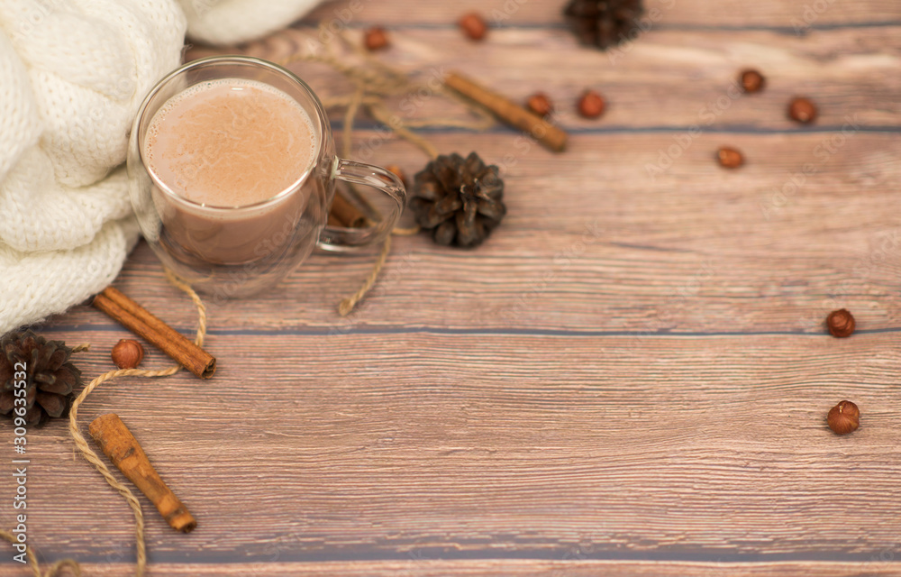 Hot cocoa in a glass cup surrounded by winter things wiyh cinnamon on wooden background. The concept of cosy holidays Hot cocoa in a glass cup surrounded by winter things wiyh cinnamon on wooden background. The concept of cosy holidays