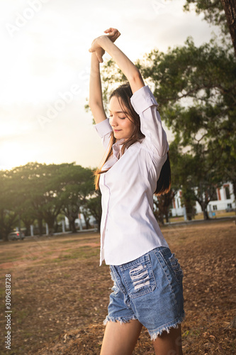 Young woman stand and stretch lazily in the morning  sun shine on her face at the park