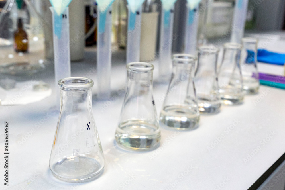 A long row of glass flasks with a clear liquid during a research experiment on a laboratory bench. The concept of modern science. A long row of glass flasks with a clear liquid during a research experiment on a laboratory bench. The concept of modern science.