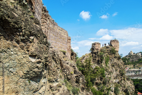 The back of the Narikala fortress-castle above Tbilisi Georgia with tourists on section with ancient towers overlooking Kura River with Holy Trinity Cathedral in distance