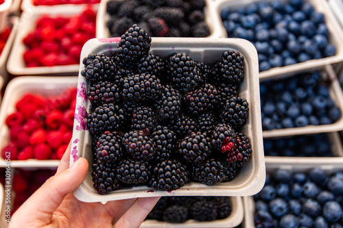 A close up and top down view as a person picks a carton full of ripe blackberries from a market stall 