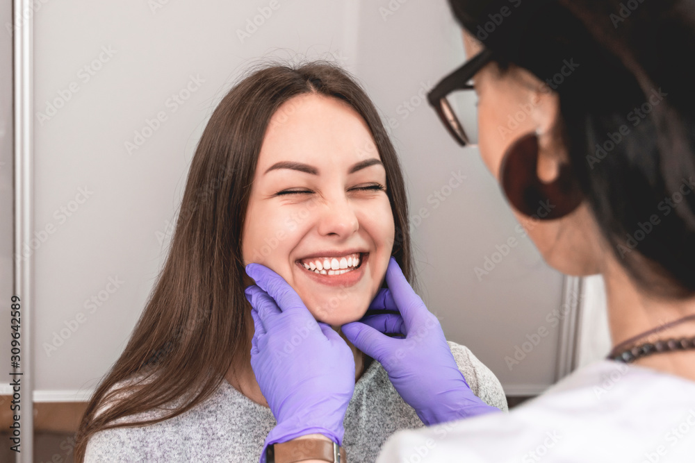 female cosmetologist examines facial wrinkles of the face of a strongly smiling patient female cosmetologist examines facial wrinkles of the face of a strongly smiling patient
