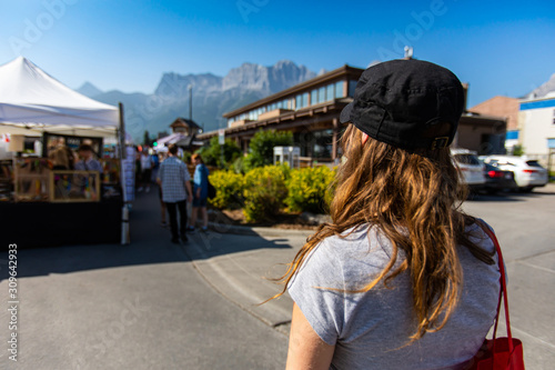 A closeup and rear view of a slim caucasian girl with brunette hair and baseball cap during a local farmers market, with copy space on the left