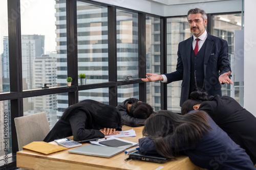 Boss bored and looking down at lazy colleague sleeping on table in meeting room photo