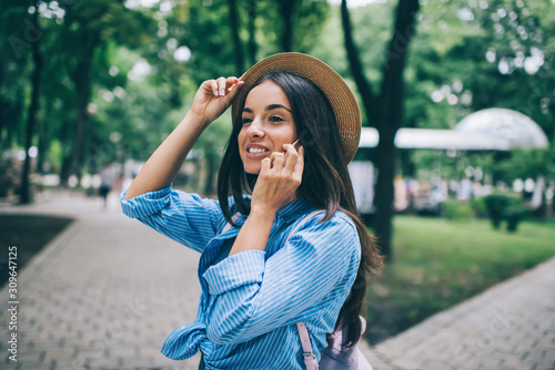 Cheerful woman with cute smile feeling good during friendly conversation via cellular phone, happy Caucasian female teenager in trendy calling to best friend for communicate rejoicing outdoors