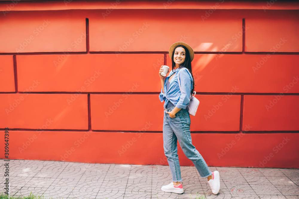 Happy excited female traveller walking around city urban setting enjoying free time for discover world, positive Ukrainian woman in trendy apparel holding takeaway cup with caffeine beverage