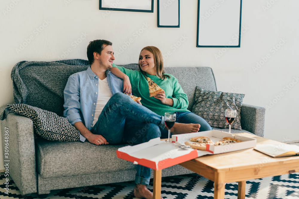 Attractive young couple relaxing on sofa eating pizza