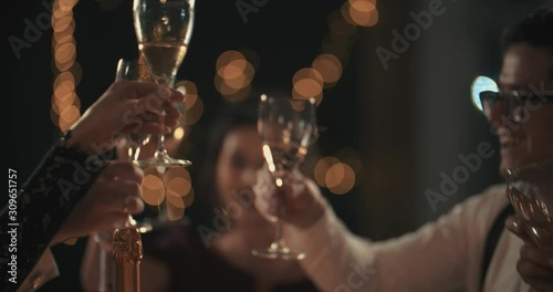 Multiracial young mans and womans wearing fashion wear clinking glasses with champagne, happy asian american and caucasian friends celebrating xmas, new year or birthday party indoors