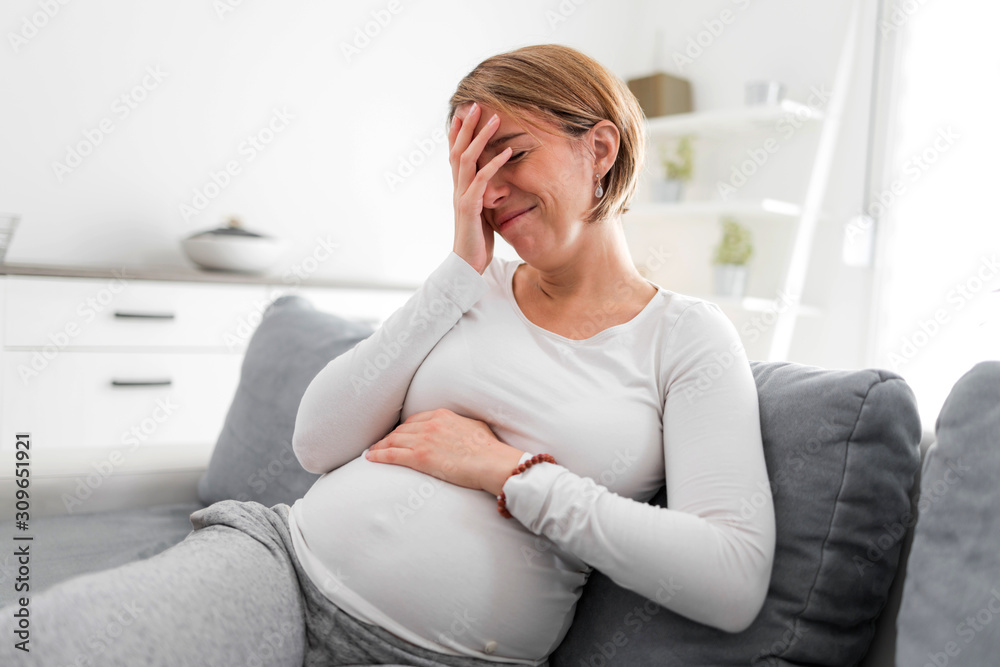 Pregnant tired exhausted woman with stomach and head issues at home on a couch, being sick. Pregnant tired exhausted woman with stomach and head issues at home on a couch, being sick.