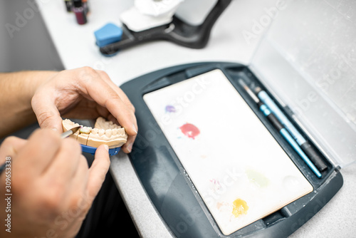 Dental technician coloring dental prosthesis with a paint brush at the laboratory, close-up view. Concept of implantats producing