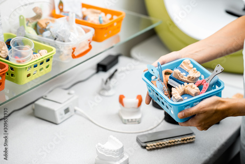 Dental technician with container full of various artificial jaw models, impressions and dental implants at the laboratory