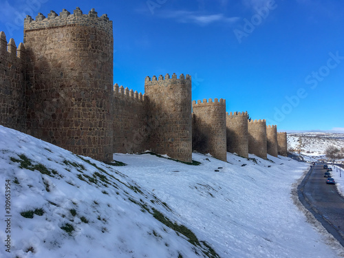 Muralla medieval de Ávila con cielo azul y nieve a sus pies en un soleado día de invierno (España).