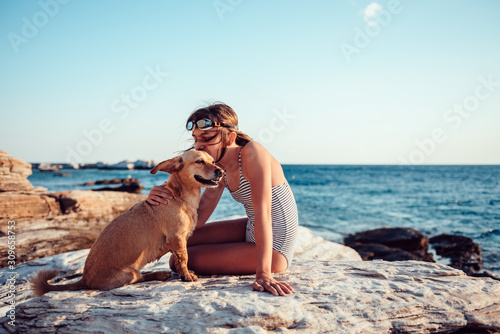 Girl kissing her dog while sitting on the rocky beach