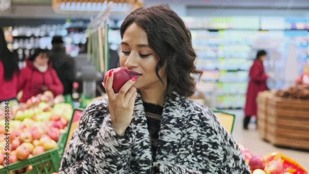 Beautiful woman looking at camera and smiling with apple in hands. African american woman buying apples in supermarket. Woman take red apple in marketplace. Vegan concept. Close-up in 4K, UHD Beautiful woman looking at camera and smiling with apple in hands. African american woman buying apples in supermarket. Woman take red apple in marketplace. Vegan concept. Close-up in 4K, UHD