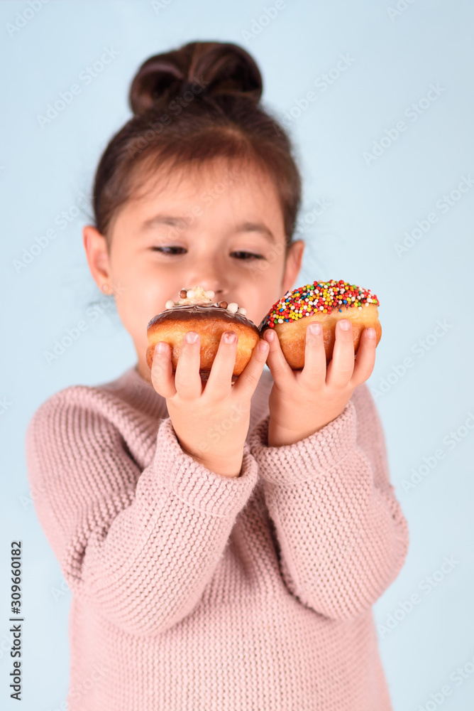 Little happy cute girl eating donuts on blue background. Child having fun with donut. Little happy cute girl eating donuts on blue background. Child having fun with donut.