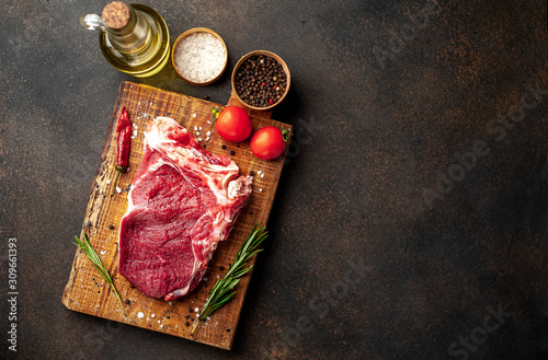 one raw steak with spices and rosemary on a stone background with copy space for your text