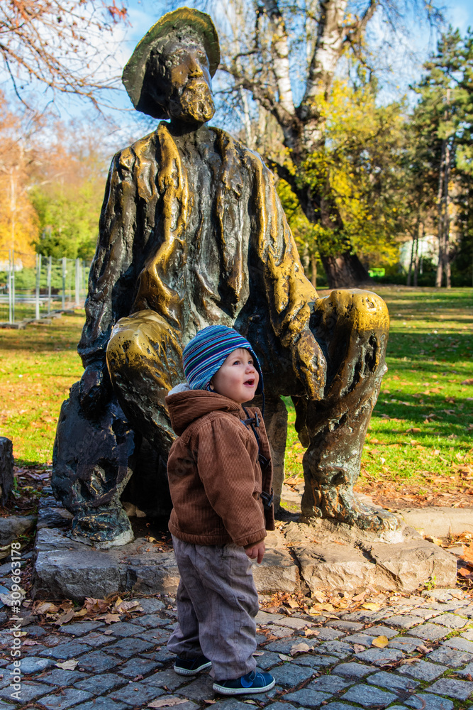 Little boy standing in autumn park. A boy stands by the monument