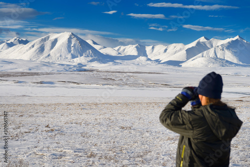 Female tourist looking at the snow covered Brooks Range mountains with binoculars from the Dalton Highway Alaska