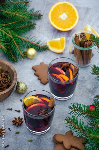 Mulled wine in a glass with orange, apple, raisins, cinnamon, star anise and other spices on a gray background with gingerbread. Fragrant hot winter drink. Christmas drink.