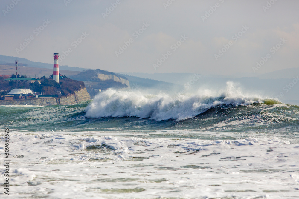 Beautiful, big storm waves at the entrance to Gelendzhik Bay. In the background, the lighthouse tower on a steep steep Bank.