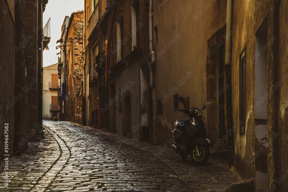 Narrow old italian street with motorcycle near the house at early sunrise in the small famous town Caltagirone in Sicily, Italy