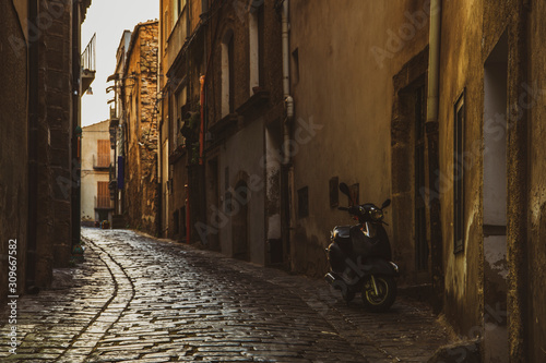 Narrow old italian street with motorcycle near the house at early sunrise in the small famous town Caltagirone in Sicily, Italy