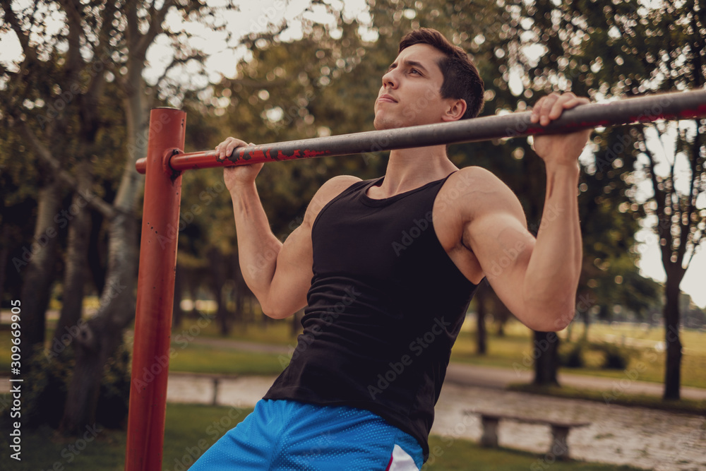 Naklejka premium Man doing chin ups on the bar in the park