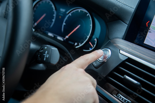 male finger presses the start stop engine button on a car dashboard. close-up, soft focus, in the background the dashboard and car speedometer in blur, side view © Maria