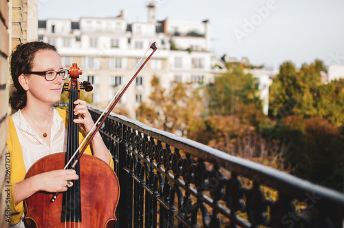 Fotografia Young smiling female cellist plucking cello strings on a beautiful balcony
