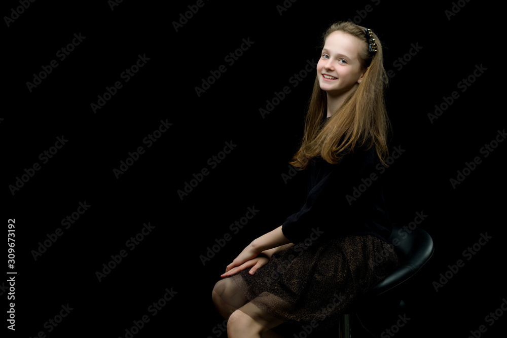 Charming girl teenager sitting on a chair in the studio on a bla Charming girl teenager sitting on a chair in the studio on a bla