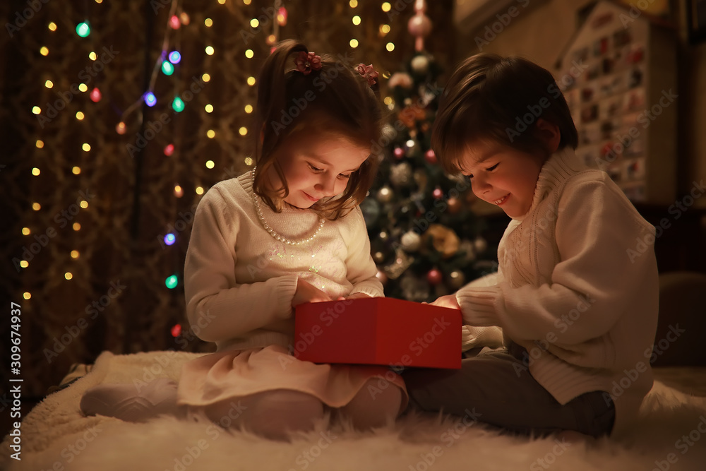 Family on Christmas eve at fireplace. Kids opening Xmas presents. Children under Christmas tree with gift boxes. Decorated living room with traditional fire place. Cozy warm winter evening at home.