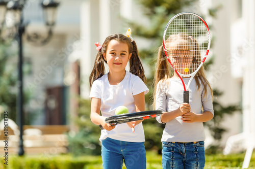 Happy preteen girls in sport outfits with tennis rackets on green grass background © Angelov