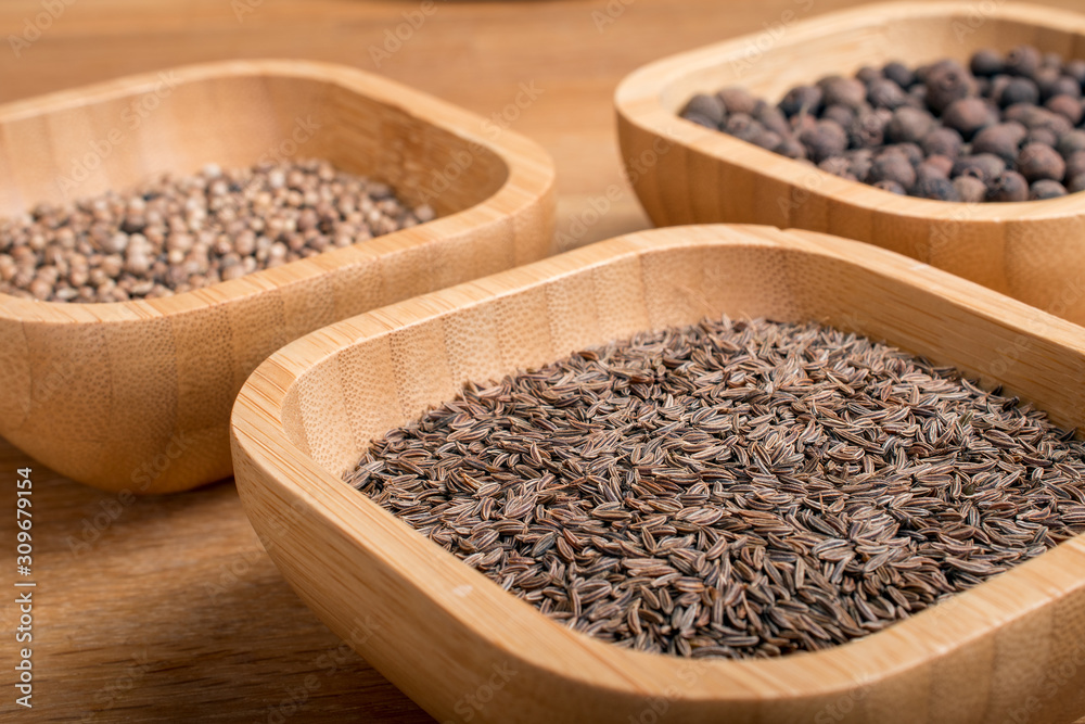 Cumin, coriander and pepper in bamboo jars on a wooden background. Cumin, coriander and pepper in bamboo jars on a wooden background.