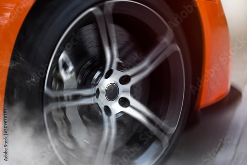 Orange Sport Car with detail on spinning and smoking wheels tires doing burnouts  dynamic photo