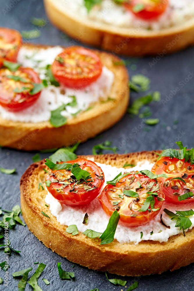 Crostini withe cream cheese, cherry tomatoes and fresh basil. Dark stone background. Close up. 