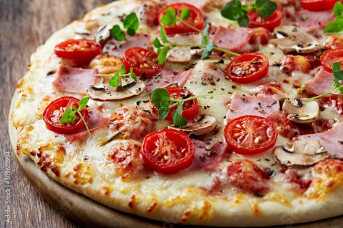 Tasty pizza with ham  cherry tomatoes  mozzarella cheese  champignon mushrooms and fresh oregano. 