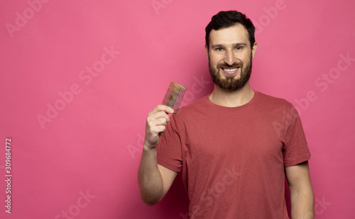Portrait of young happy attractive hipster male and confident look, holding wooden comb on pink background.