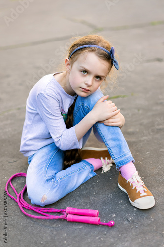 Frightened youg girl sitting on the pavement with skipping rope looking towards camera photo