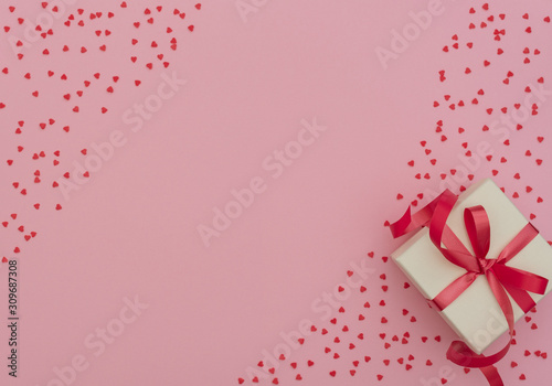 Valentine's Day concept. White gift box with red ribbon on pink background with lots of small red hearts. Valentine greeting card. Flat lay style with copy space. © Rina Mskaya