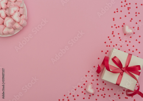 White gift box with red ribbon and heart-shaped marshmallows in white bowl on pink background with lots of small red hearts. Valentine's Day concept, greeting card. Flat lay style with copy space. © Rina Mskaya
