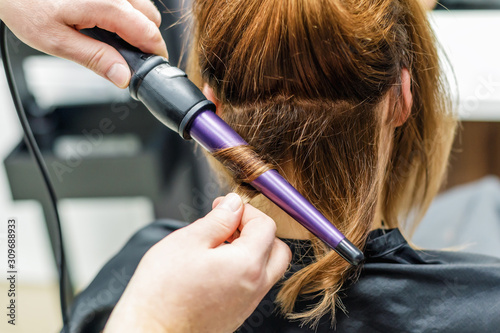 Hairdresser make hair wavy for woman with electric hair curler, closeup.