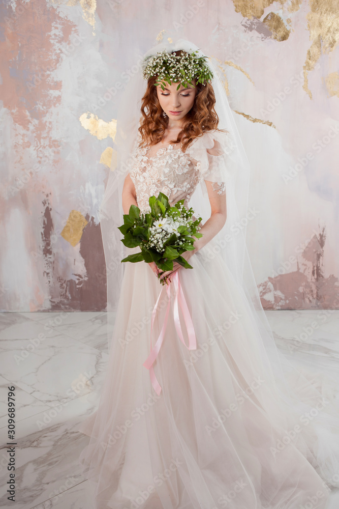 Portrait of a young beautiful woman in wedding dress with wreath and bouquet of fresh flowers.