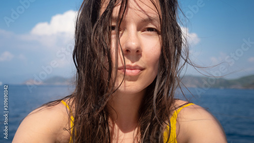Vacation at the sea, young woman with wet hair after swimming, close-up portrait.