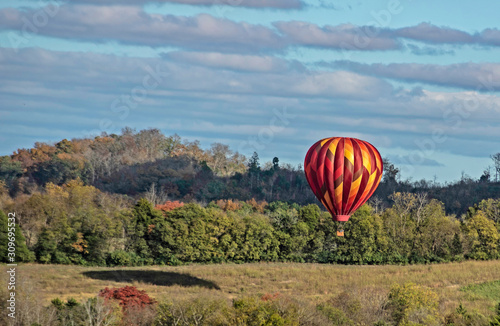 A single hot air balloon flies over a green valley.